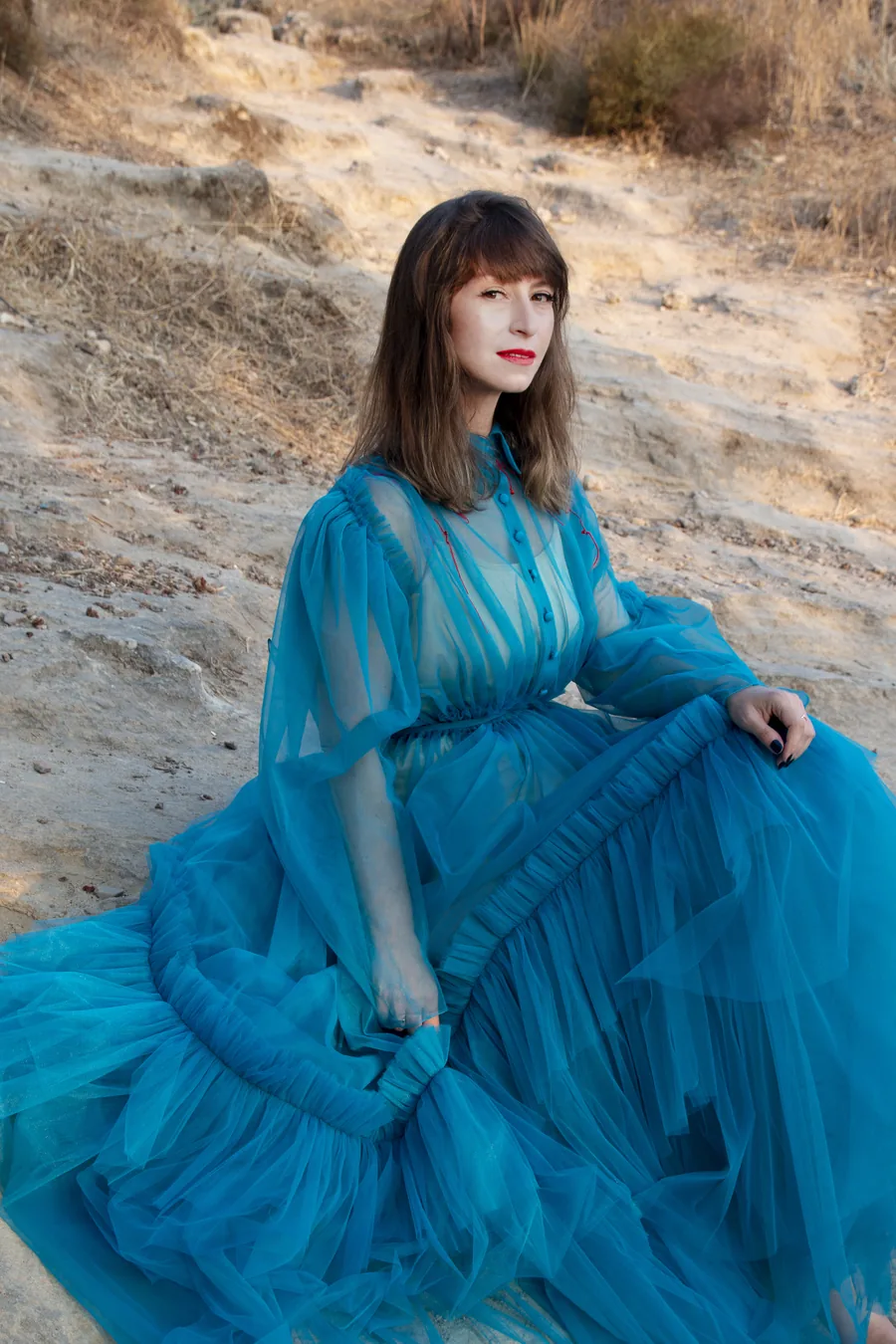 Aviya Kopelman in a teal gown on dry ground, looking at the camera